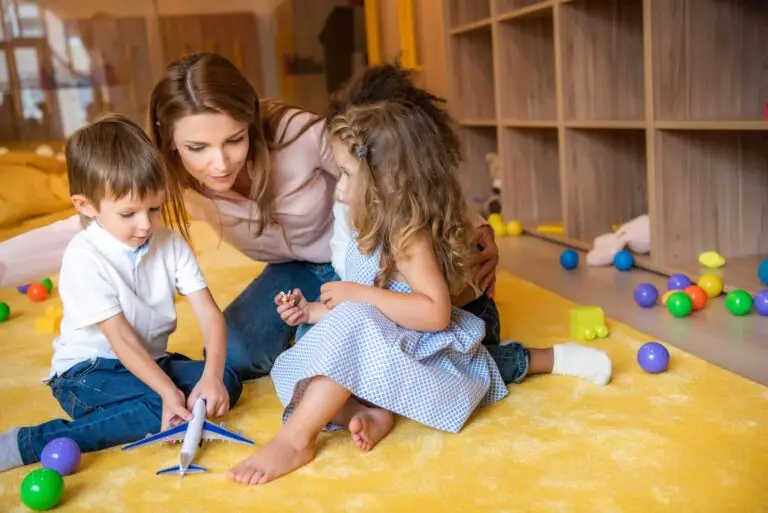 tutor hugging adorable kids on carpet in kindergarten